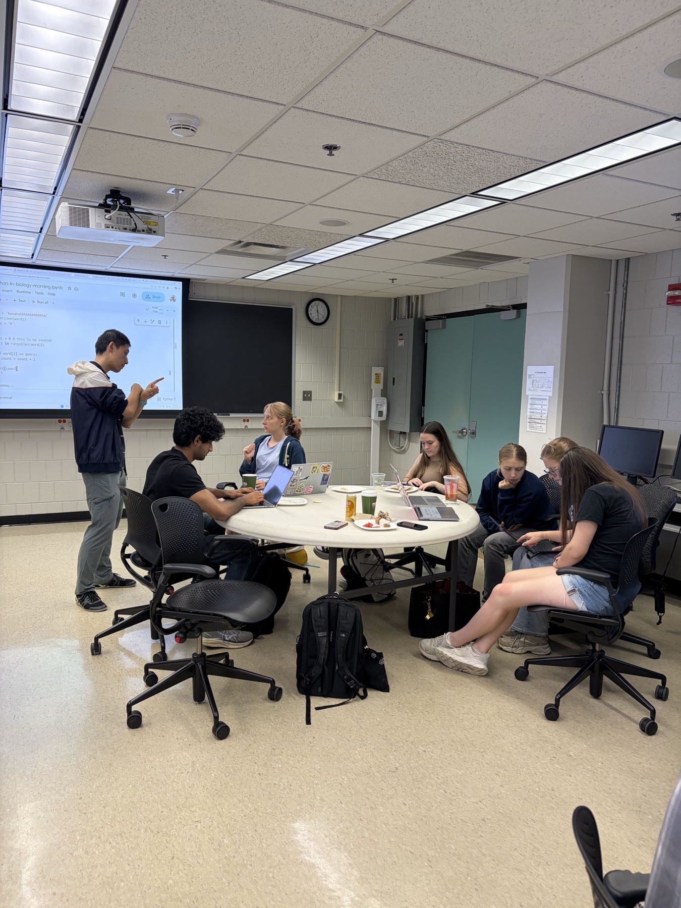 An instructor checks in with a student team during a coding exercise